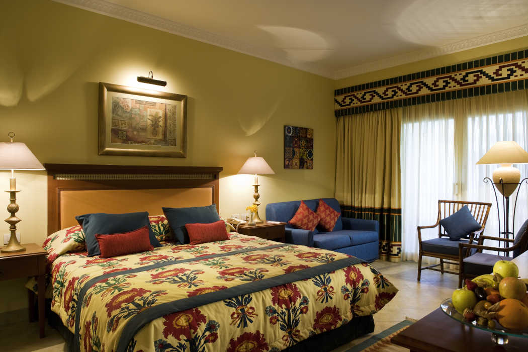 The luxury king bed in blue and beige decoration and a touch of red in pillows at Mosaique Beach Resort in Taba Egypt