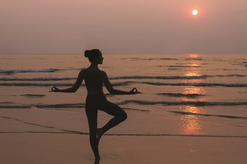 woman practicing yoga pose on the beach sunrise sunset